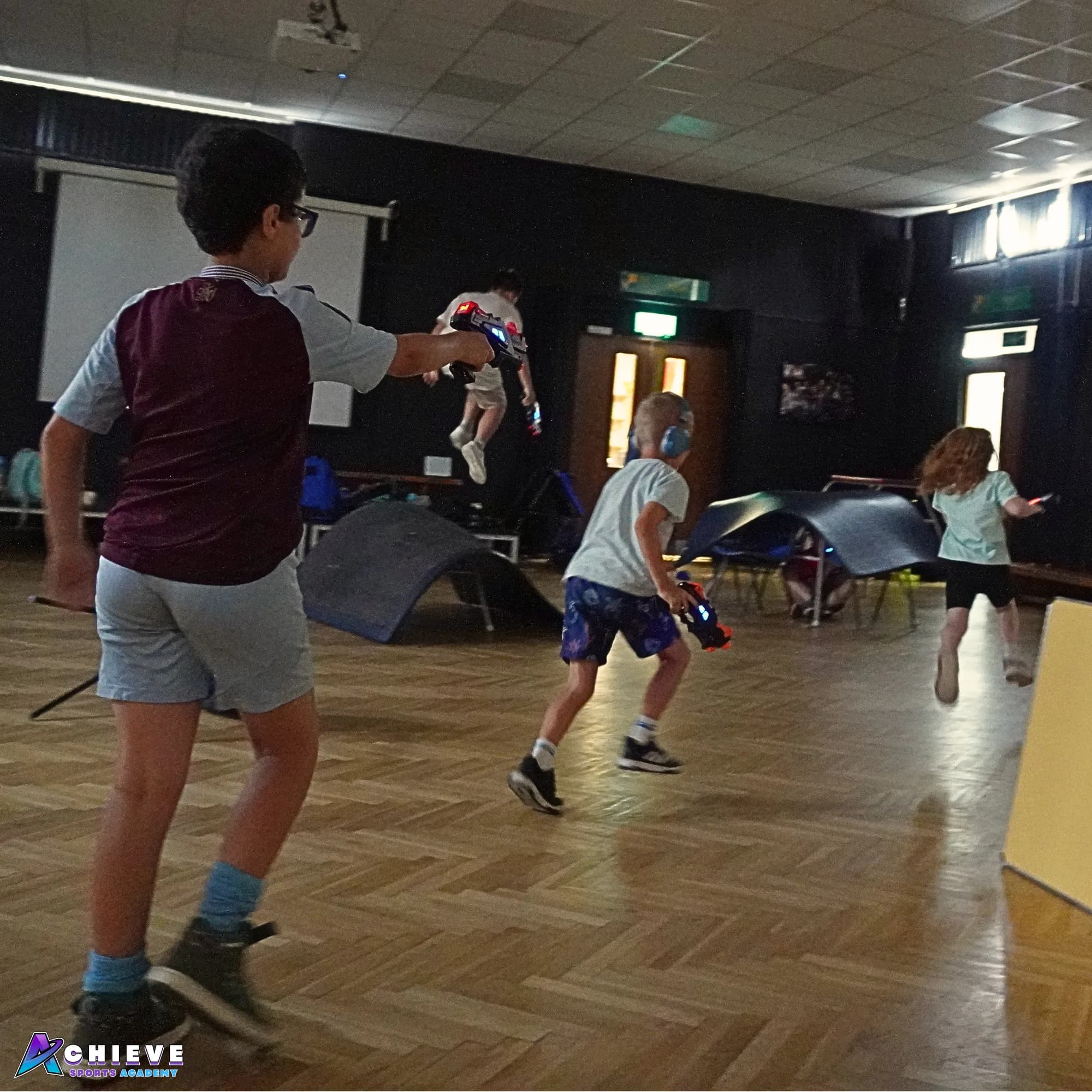 Children dodging between obstacles during a blaster battle in the school hall