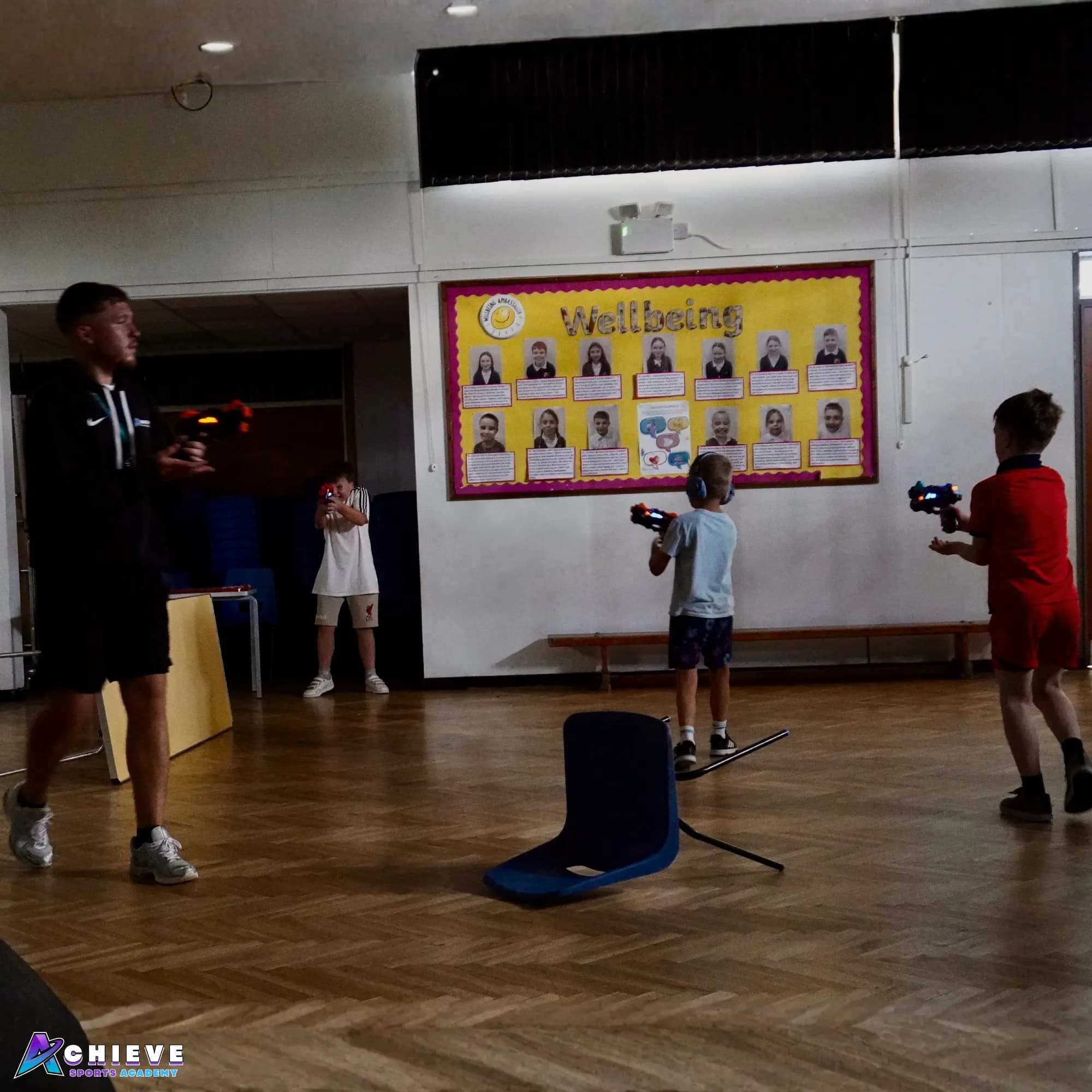 Children playing a laser tag team game in a school hall with an Achieve coach
