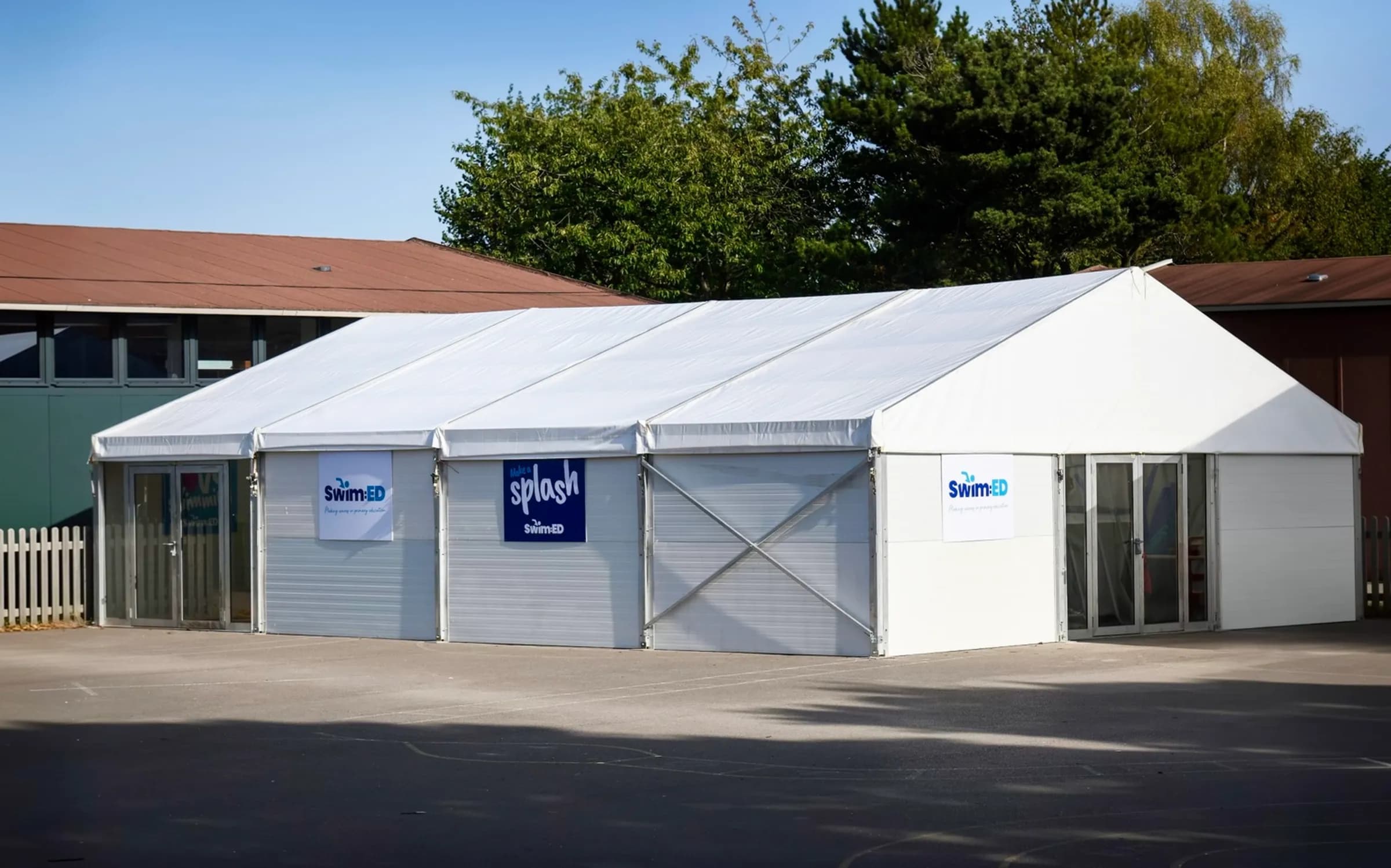 Swim:ED enclosed pool structure with rigid wall panels and glazed entrance doors on a school site