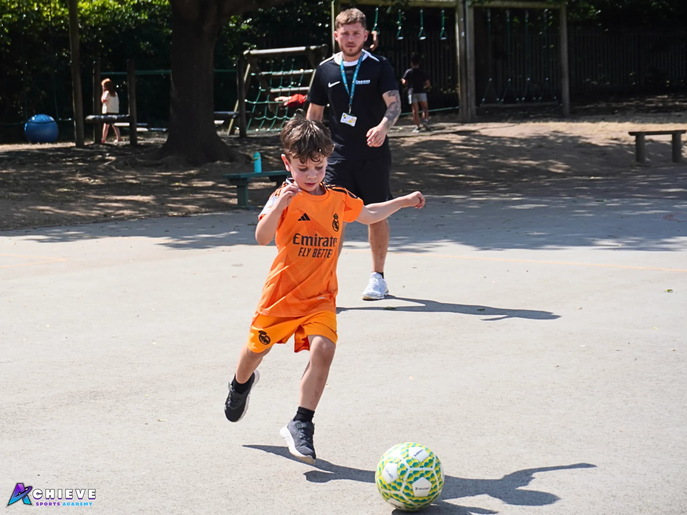 Achieve Sports Academy coach supporting a child during an outdoor football session